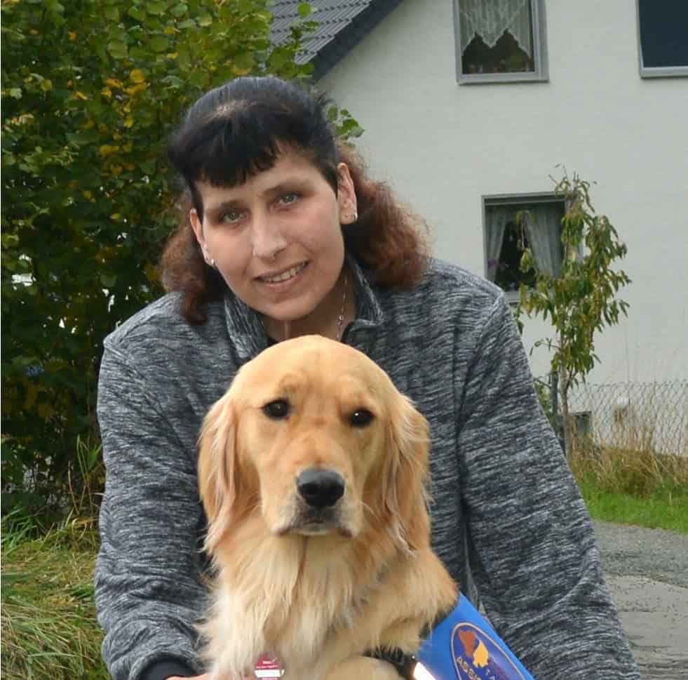Angela mit ihrem Hund vor einem Haus.