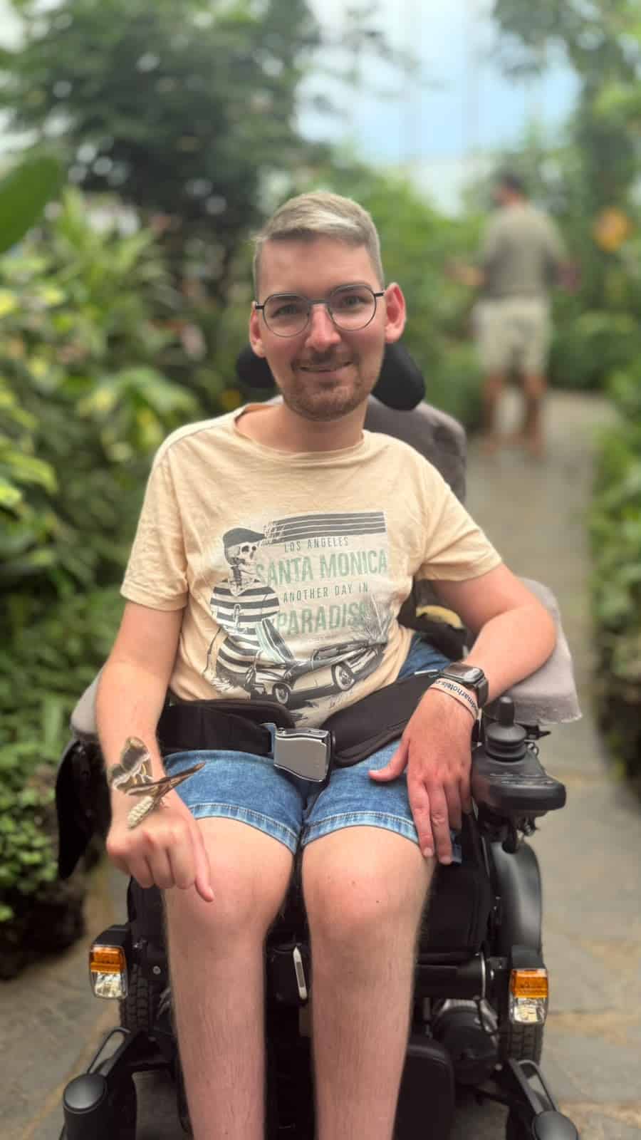 Eine männlich gelesene Person in Shorts und T-Shirt sitzt im E-Rolli.